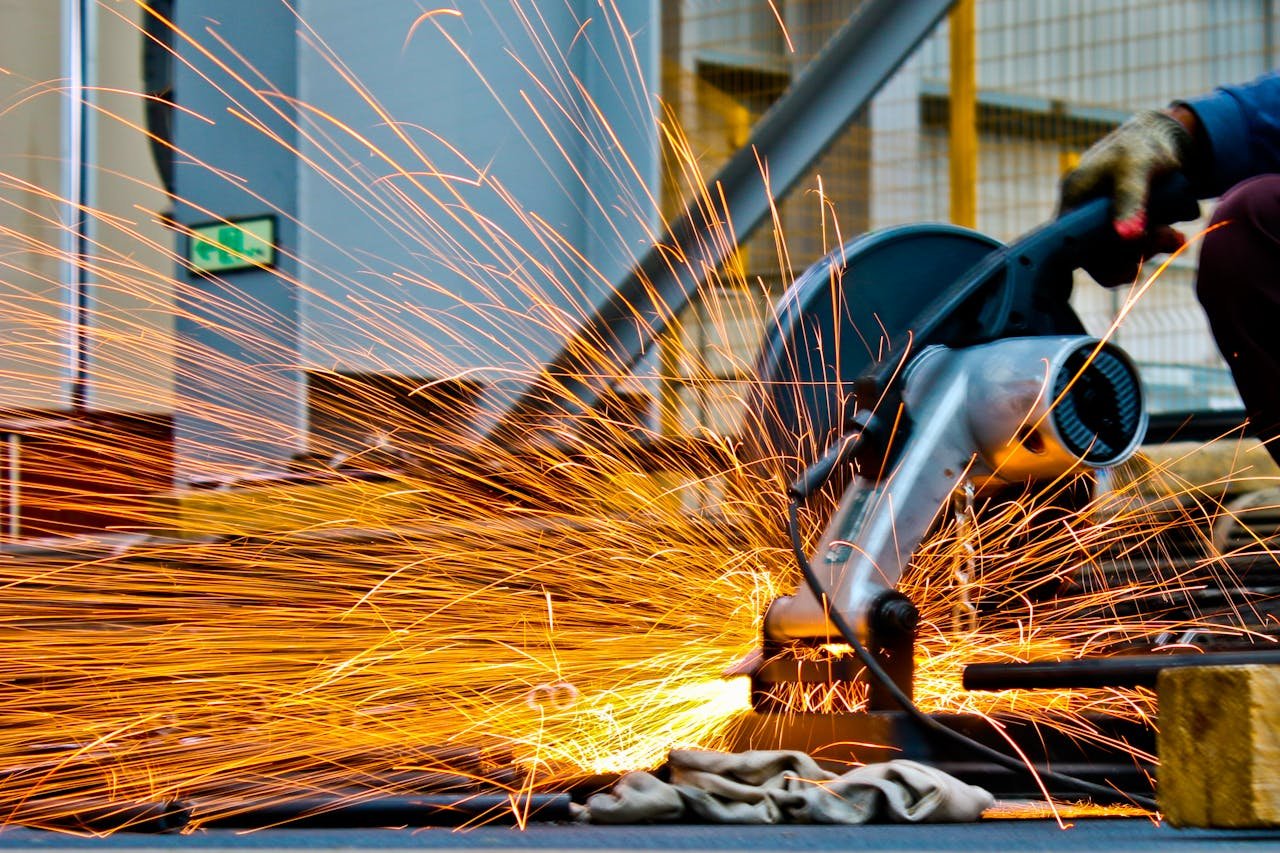 services-05 A worker operates a grinder cutting metal, creating a vibrant display of sparks in an industrial setting.